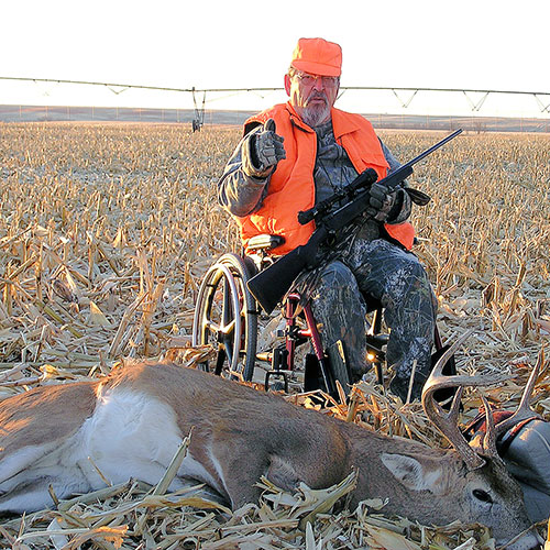 Hunter in wheelchair gives thumbs up in field as he poses in front of his trophy
