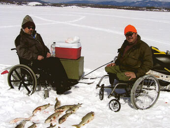 Duo of hunters in wheelchairs pose in front of their fish on ice and snow