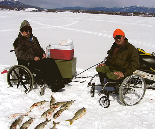 Duo of hunters in wheelchairs pose in front of their fish on ice and snow