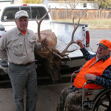 Two men standing in front of truck with their trophy animal in the back of the truck