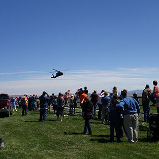 Large gatgering of people in an open field with a helicopter flying above