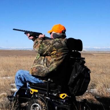 Man in wheelchair aiming down sights of rifle in a field