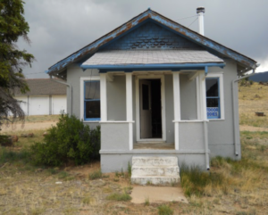 Worn house with blue roof and gray shingles with front door open